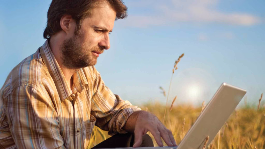 Farmer sitting in a field with a laptop open