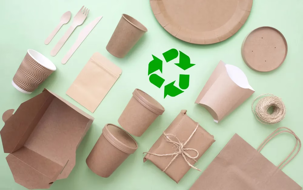 Collection of sustainable packaging materials against a light green background with a recycle sign.
